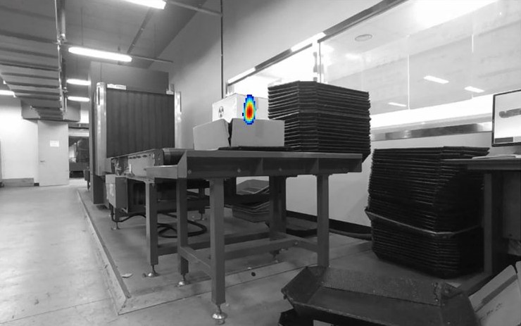 Live camera view of a customs warehouse with the reconstructed radiation hotspot drawn on a box on the conveyor table.